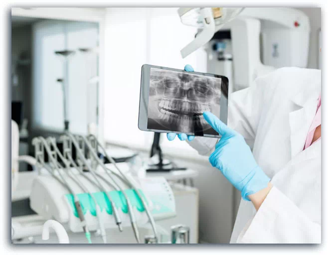 Stomatolog wskazuje palcem na tablet ze zdjęciem rtg zębów