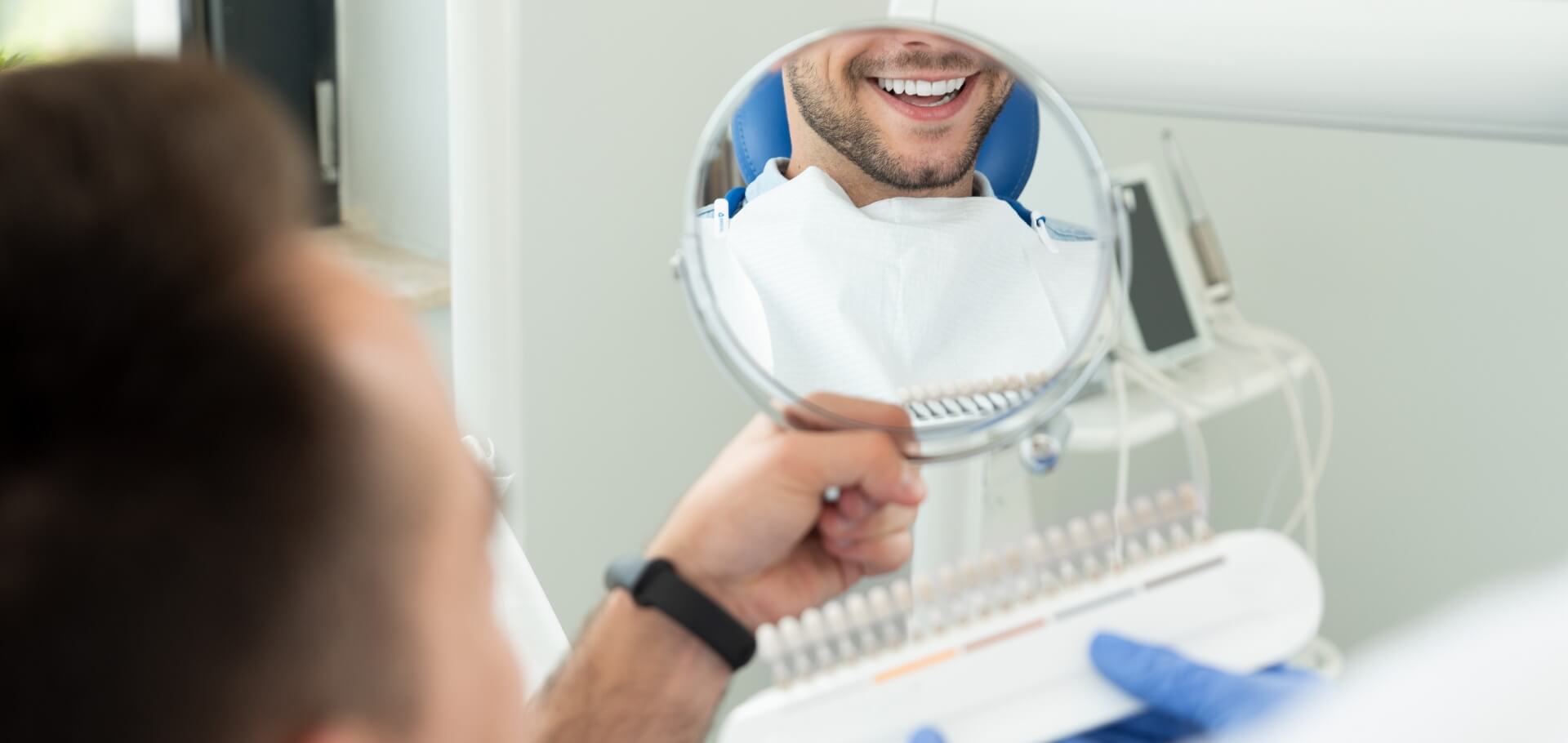 Stomatolog pokazuje próbki implantów uśmiechniętej osobie Slajd #3